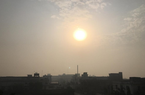 अशोकनगर शहर के ऊपर सुबह के सूर्योदय का एक सुंदर दृश्य है। आसमान में सूरज एक चमकदार गोले की तरह दिख रहा है, जो हल्की धुंध या कोहरे के पीछे से चमक रहा है। अग्रभूमि में शहर की इमारतों और घरों की काली परछाइयाँ दिखाई दे रही हैं। यह दृश्य सुबह की शांति और हल्की ठंड के मौसम को दर्शाता है।